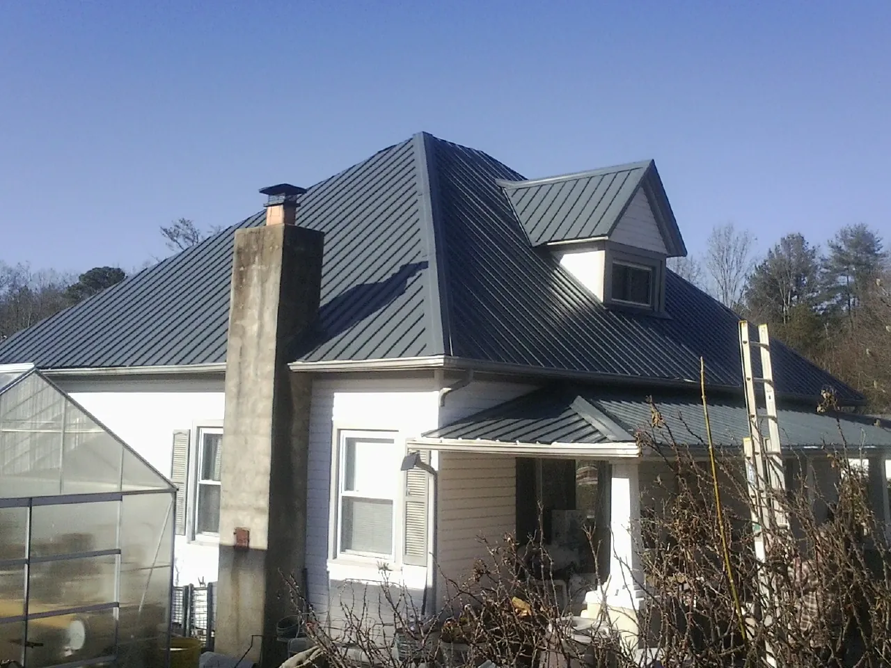 Dark blue standing seam metal roof on a white farmhouse with dormer — Slate & Tile Roof Repair by Roofing Brothers in Fort Scott