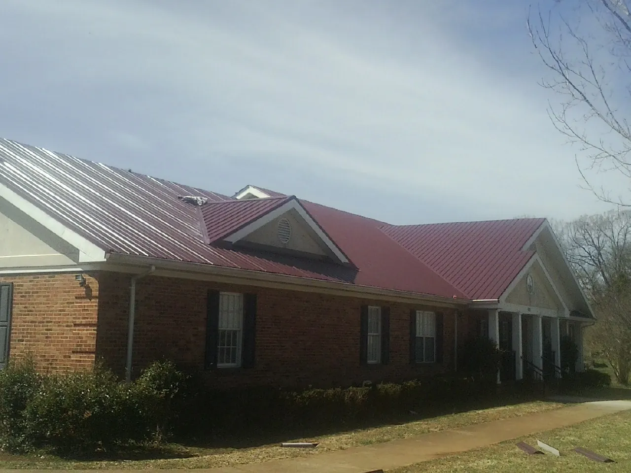 Red metal roof with gabled entries on a long brick building, from a Hail Damage Roof Repair job in Fort Scott