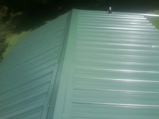 New green metal panels meeting at the ridge of a roof — Flat Roof Repair work by our crew in Fort Scott