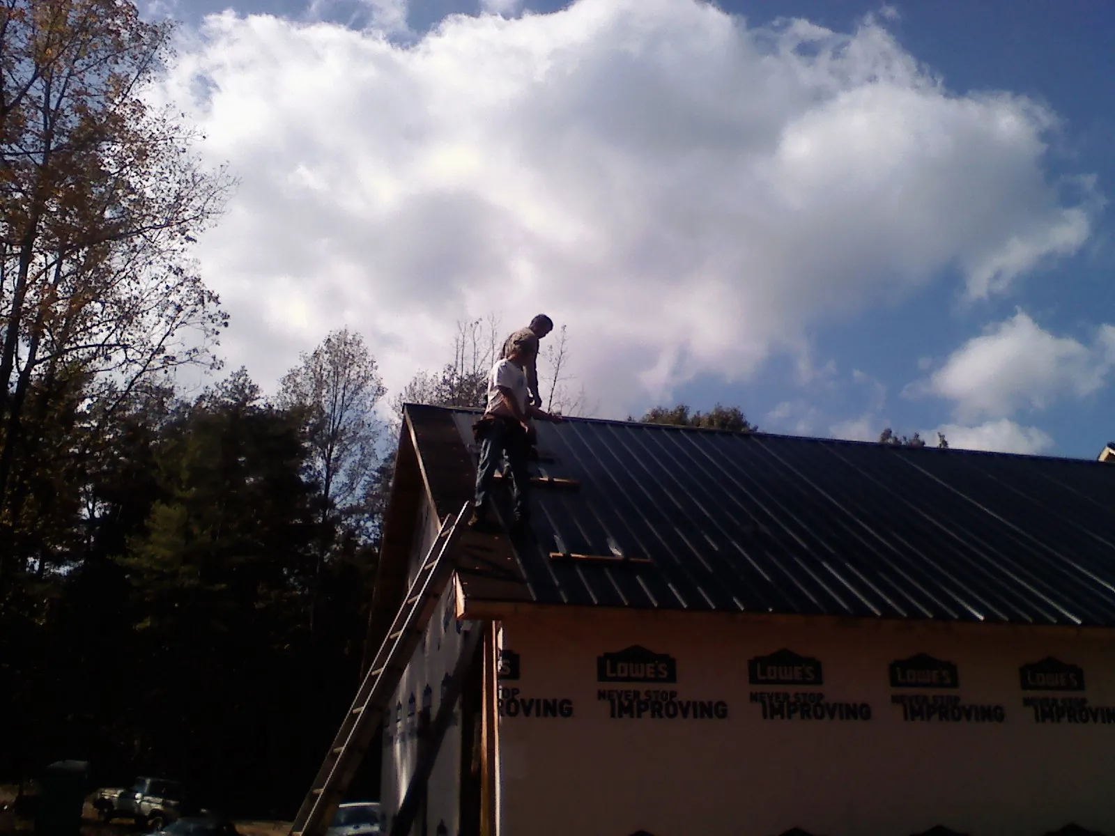 Roofer fastening dark metal panels high against a cloudy sky, from a Roof Inspection job in Fort Scott