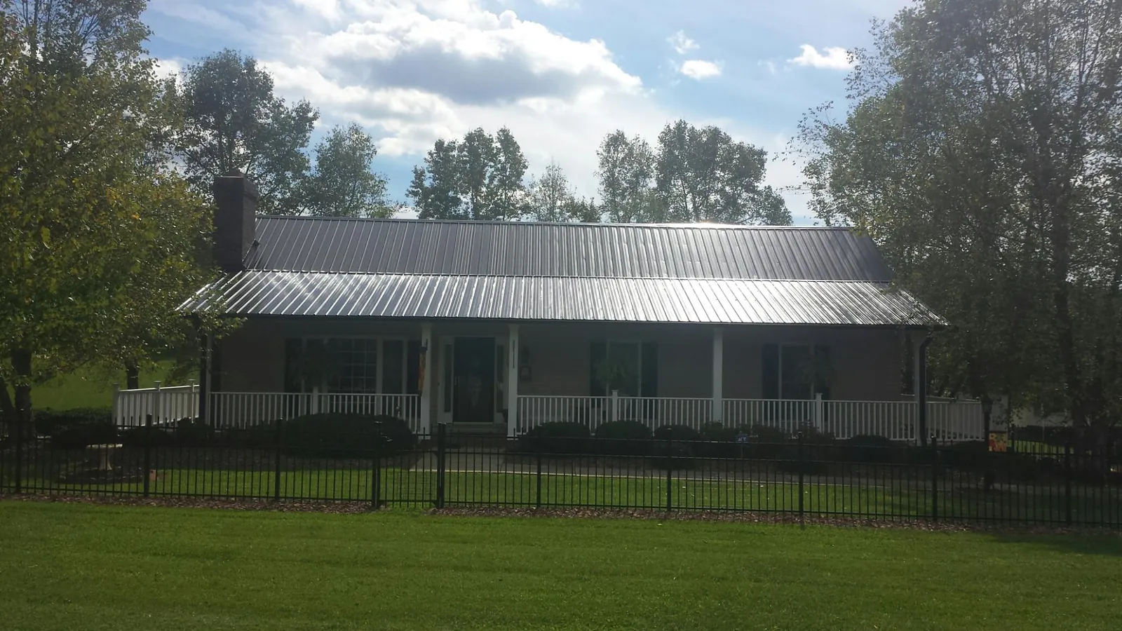 Gray metal roof on a brick ranch with a full width front porch — Gutter Guard Installation work by our crew in Fort Scott