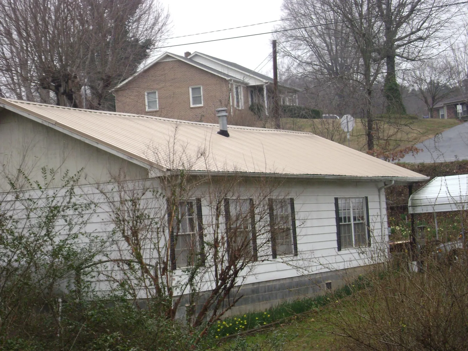 Tan metal roof on a white sided house set into a hillside — Commercial Roofing by Roofing Brothers in Fort Scott