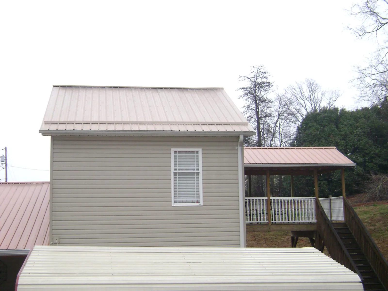 Tan metal roofs on a two story addition and attached porch, from a Roof Replacement job in Fort Scott